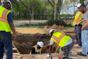 Team of construction workers inspecting an underground utility site on a sunny day.